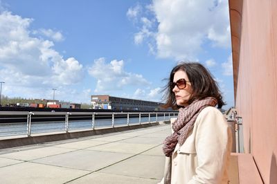 Side view of young woman in sunglasses standing on promenade during sunny day