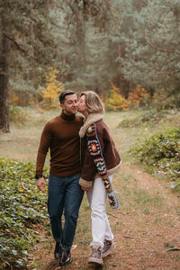 Woman is kissing man on cheek while walking through forest, happy couple spending time together