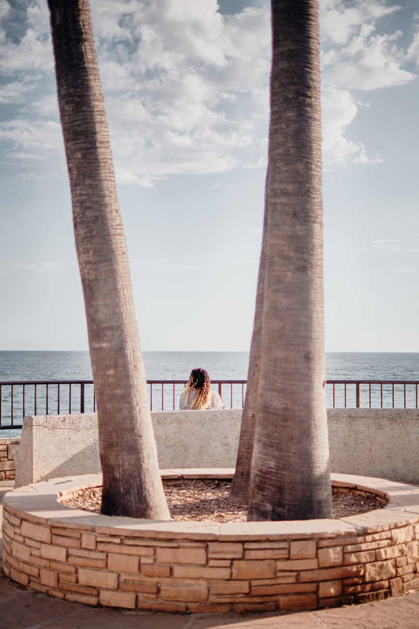 sky, nature, water, sea, architecture, cloud, adult, one person, wood, architectural column, day, column, ancient history, beach, women, leisure activity, travel destinations, horizon, horizon over water, land, built structure, men, travel, landmark, sculpture, standing, outdoors, full length, lifestyles, temple, vacation, rear view, trip, beauty in nature, tranquility, monument, relaxation, holiday, tourism, young adult, scenics - nature, tranquil scene