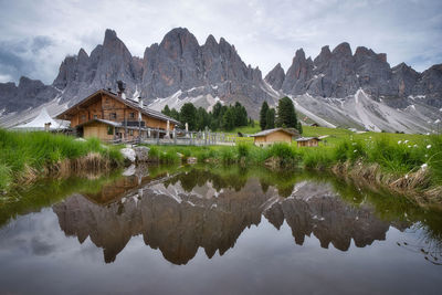 Reflection of house on lake and mountains against sky