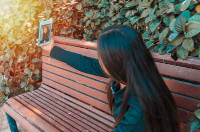 Young woman taking selfie on bench by plants