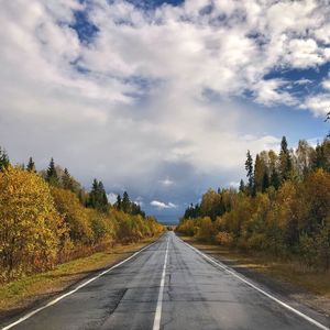 Empty road amidst trees against cloudy sky