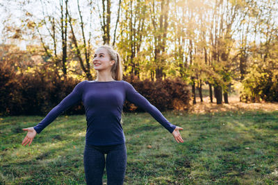 Beautiful smiling girl at morning gym in the park, looking away with arms extended.