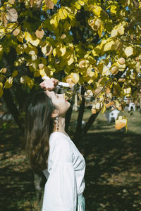 Side view of young woman with eyes closed standing by tree in park during sunny day