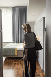 Rear view of businesswoman with luggage standing in hotel room