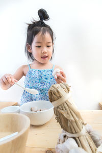 Cute girl holding garlic bulb by bowl on table against white background