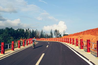 Boy riding bicycle on road against sky during sunny day