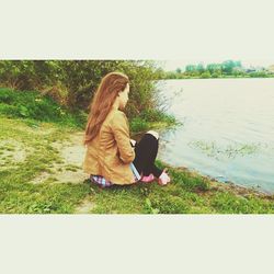 Young woman sitting on grass against sky