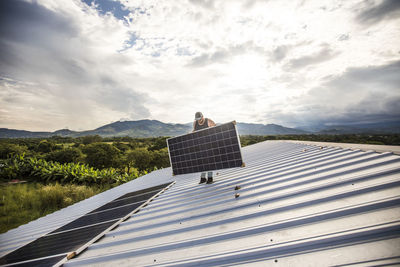 Electrician lifting solar panel into place on roof.