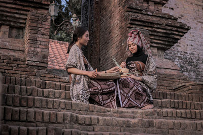 Young woman sitting against brick wall