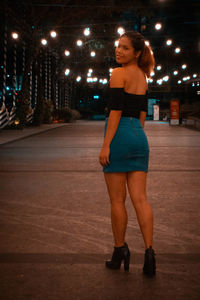 Full length portrait of young woman standing in city at night