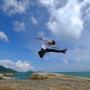 Full length of young man jumping against sea and sky