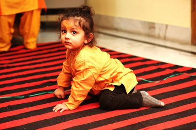 Close-up of baby girl looking away while kneeling on carpet at home