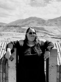 Overweight woman wearing sunglasses standing against mountains