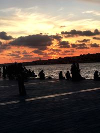 Silhouette people on beach against sky during sunset