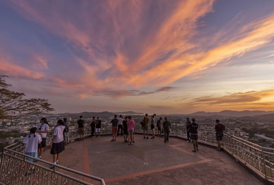 People walking on railing against sky during sunset