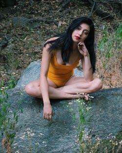 Sensuous young woman sitting on rock in forest