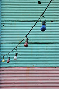 Close-up of light bulbs hanging against corrugated iron