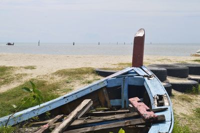 Abandoned boat on beach by sea against sky