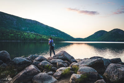 Man standing on rock by lake against sky