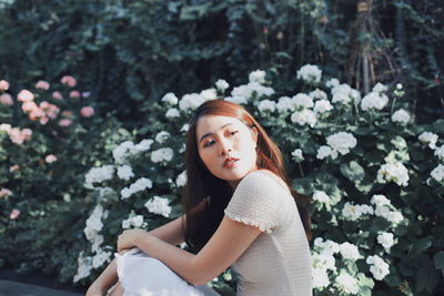 Beautiful young woman looking away while sitting against plants