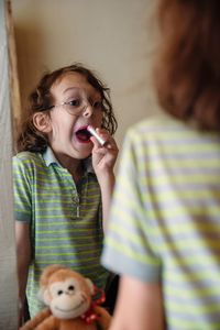 Boy with applying lipstick while looking in mirror