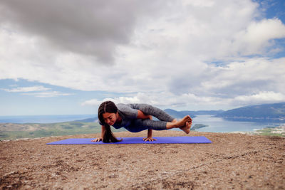 Woman exercising on mountain against cloudy sky