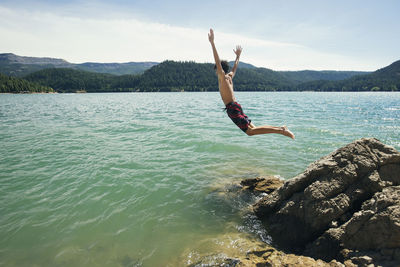 Side view of boy jumping into lake against sky