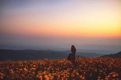 Woman standing on field against sky during sunset