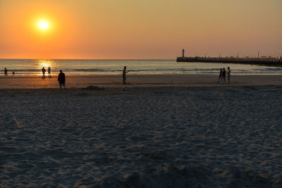 Silhouette people on beach against sky during sunset