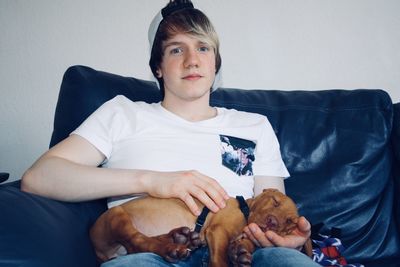 Portrait of man holding dog while sitting on sofa at home