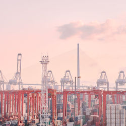 Cranes at harbor against sky during sunset