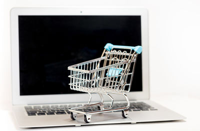 Laptop and shopping cart against white background