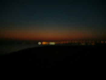 Defocused image of illuminated sea against sky at night