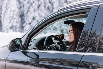 Woman driving in winter in a moutain area, while on road trip.