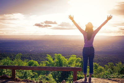 Man with arms outstretched standing on landscape against sky