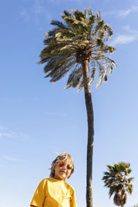 Boy wearing sunglasses standing in front of palm tree on sunny day