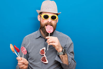 Portrait of man holding sunglasses against blue background