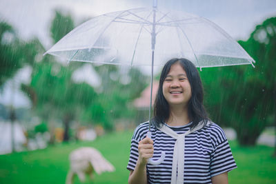 Portrait of a smiling young woman standing on rainy day