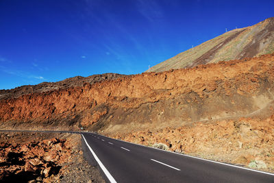 Empty road along rocky landscape against blue sky