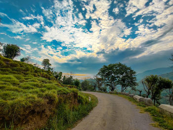 Road amidst trees on field against sky