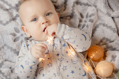 A baby boy lies on the bed and plays with a christmas garland.