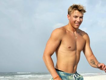 Portrait of shirtless young man standing against sea
