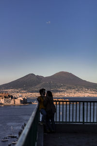 Rear view of people standing on railing against clear sky