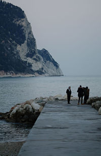 People on rocks by sea against clear sky