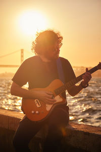 Side view of man playing guitar at sunset
