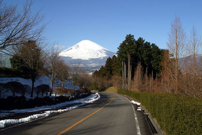 Road leading towards snowcapped mountains against clear sky