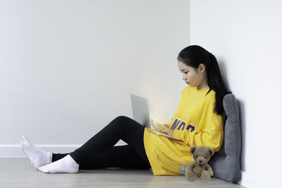 Side view of young woman sitting against wall