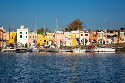 Sailboats moored in river by buildings against clear sky