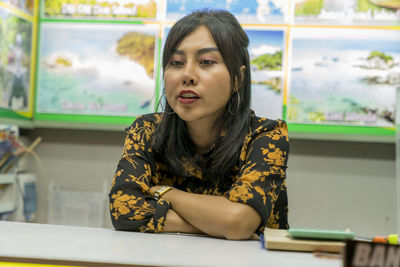 Portrait of young woman looking away while sitting on table